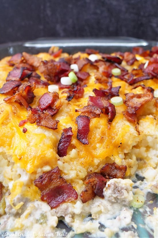 A close up photo of breakfast casserole in a baking dish, showing the layers of eggs, tater tots, cheese, and bacon.