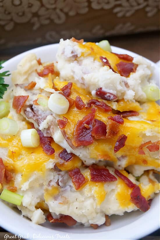 A white bowl with a serving of mashed potatoes with cheese, bacon and onions.