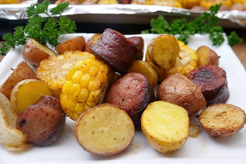 A landscape photo of a white plate with roasted potatoes, smoked sausage, and corn.