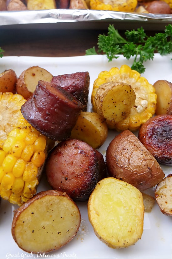 Roasted potatoes, corn, and slices of sausage on a white plate.