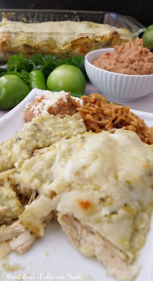 A white plate with enchilada, rice and beans on it.