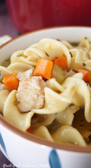 A close up of a white bowl with chicken, egg noodles and veggies in it.
