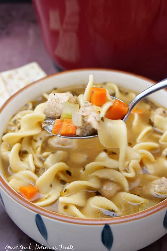 A white soup bowl with homemade chicken noodle soup in it with a spoon getting a bite out of the bowl.