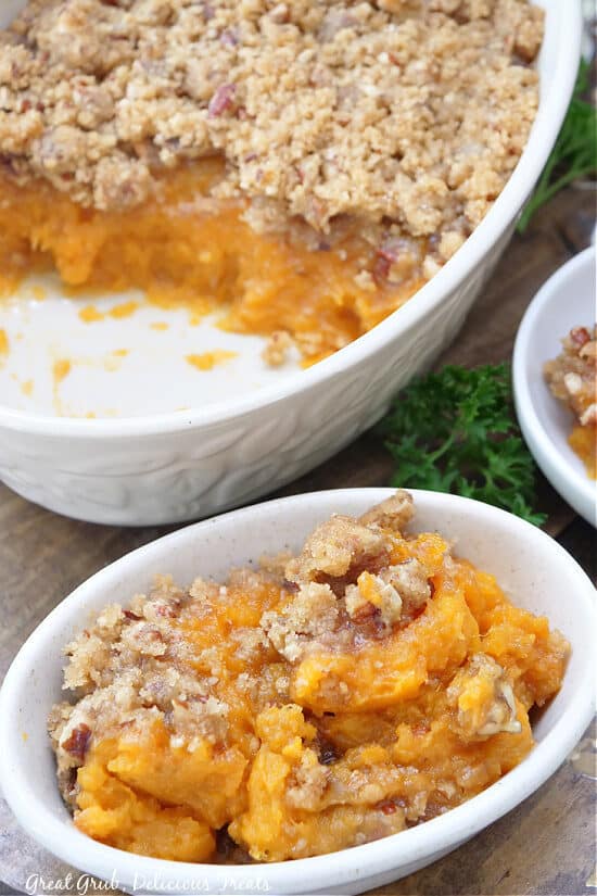 An oval serving bowl with sweet potato casserole in it and the baking dish in the background.