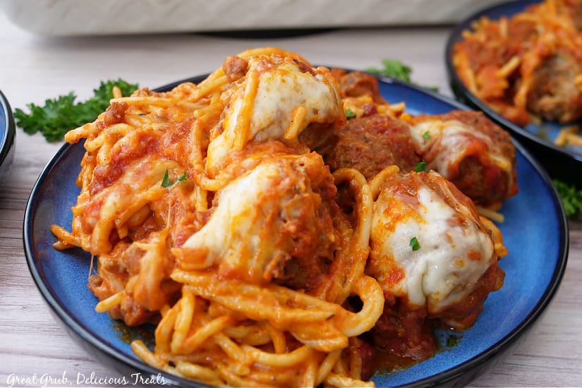 A round blue plate with 5 meatballs and cheesy spaghetti on it.