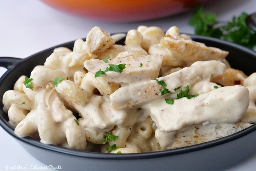 A horizontal photo of a black oval bowl with creamy chicken alfredo pasta in it.