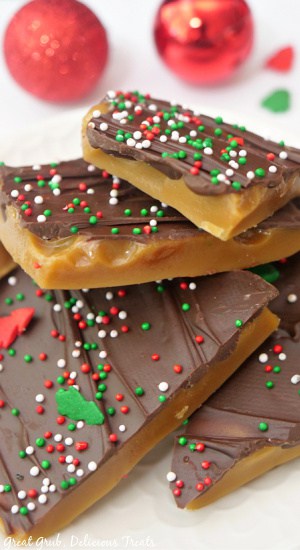 Four pieces of Christmas crack toffee on a white surface with two red mini ornaments in the background.