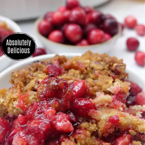 A serving of cranberry cobbler in a small white bowl and a bowl of cranberries in the background.