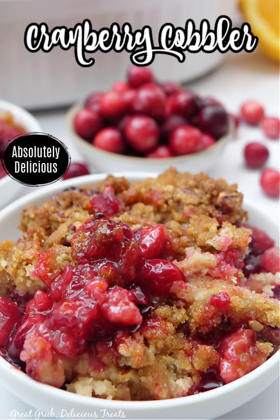A serving of cranberry cobbler in a small white bowl and a bowl of cranberries in the background.