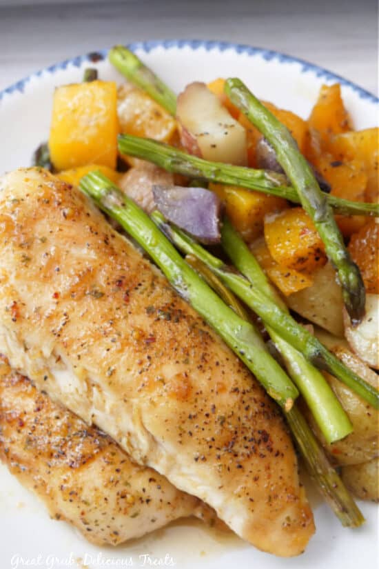 Chicken tenders, asparagus, butternut squash and potatoes on a white plate with blue trim.