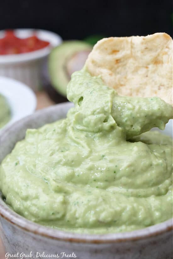 A close up of a tortilla chip being dipped into a small grey bowl filled with avocado dip.