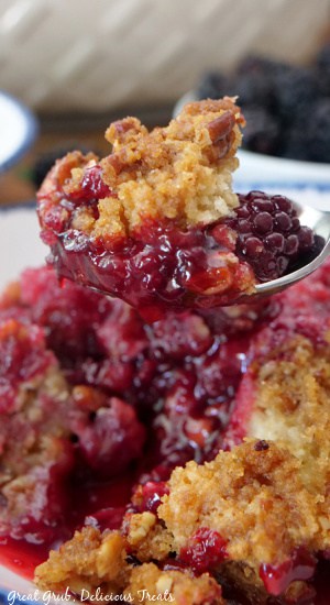 A close up of a spoonful of blackberry cobbler held above the serving bowl of cobbler.