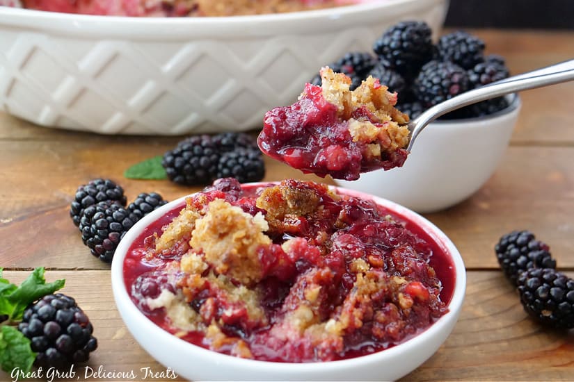 A white bowl with a serving of blackberry cobbler in it with a spoonful of cobbler scooped out of the bowl.