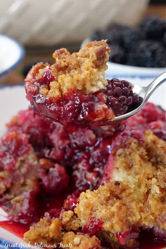 A close up of a spoon filled with a bite of cobbler on it.