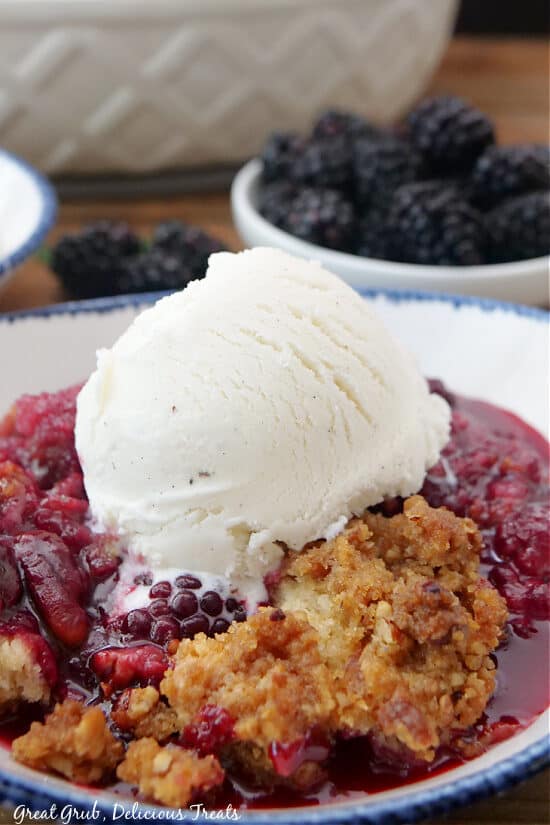 A white bowl with blue trim with a serving of cobbler and a scoop of vanilla ice cream on top of it.