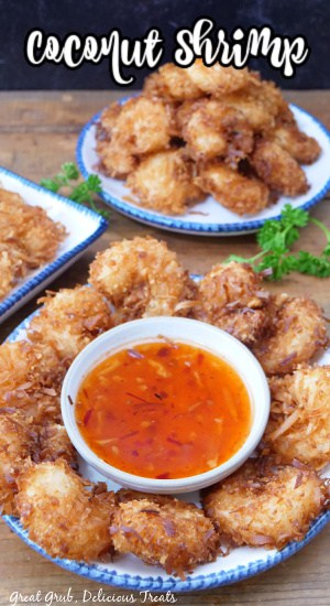 Coconut shrimp on a round white plate with blue trim with a small white bowl filled with sweet chili sauce.