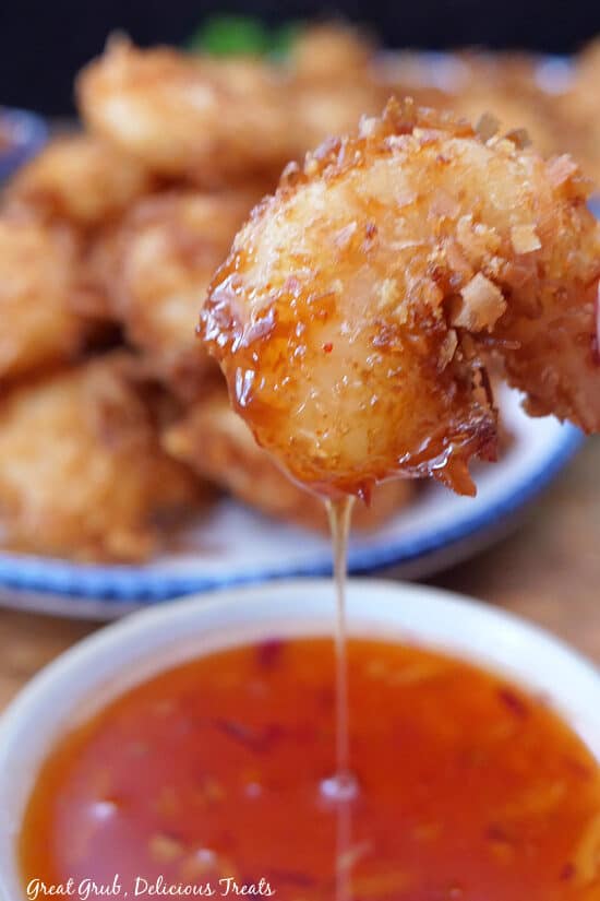A close up of a coconut shrimp that has been dipped in sweet chili sauce.
