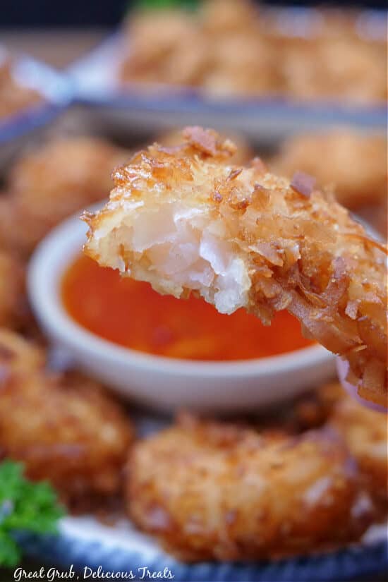 A close up of a fried coconut shrimp with a bite taken out of it.