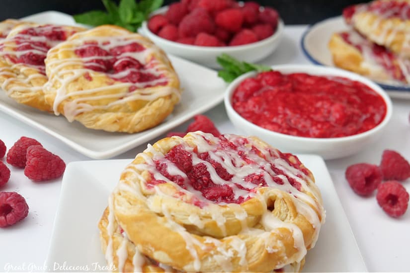 A horizontal photo of raspberry Danishes on white plate with fresh raspberries in the background.