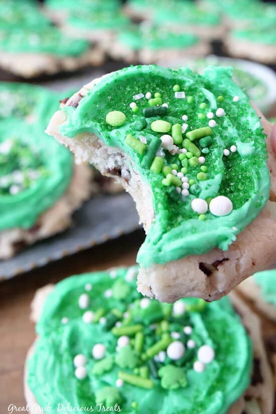 A close up of St Patricks Day cookies with green frosting and candy sprinkles with a bite taken out ft it.