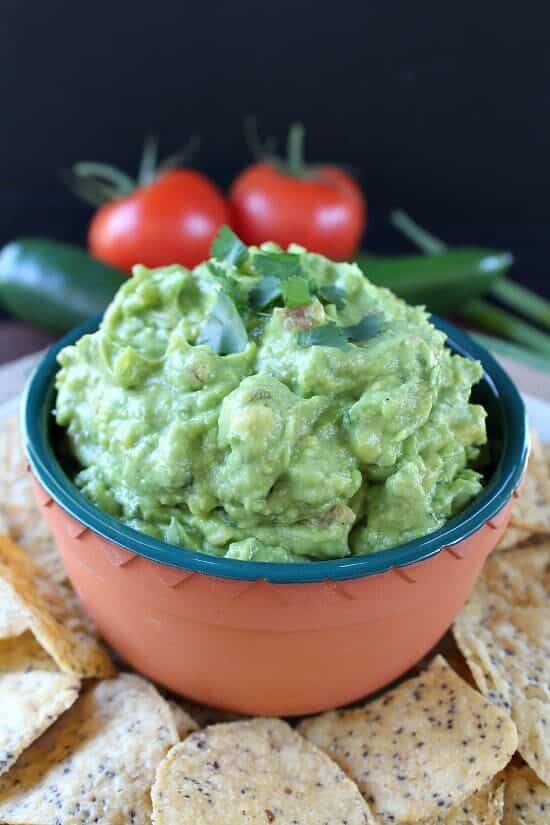 A small bowl with a serving of guacamole with a tortilla chip after it's been dipped in the guacamole.