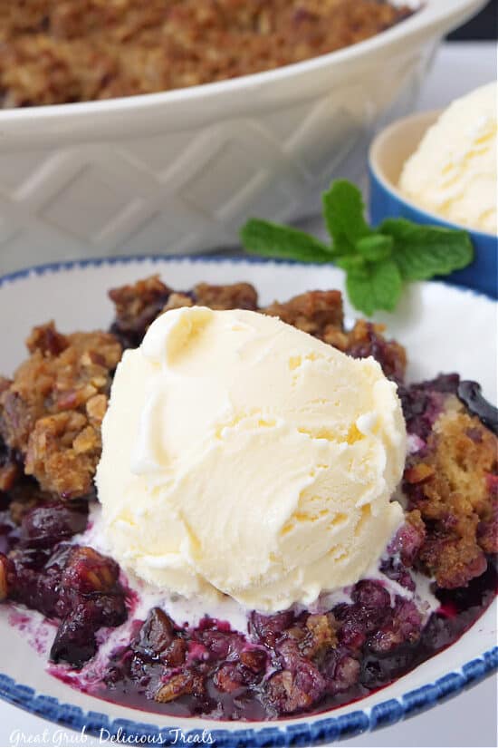 A serving bowl filled with blueberry cobbler with a scoop of vanilla ice cream on top.