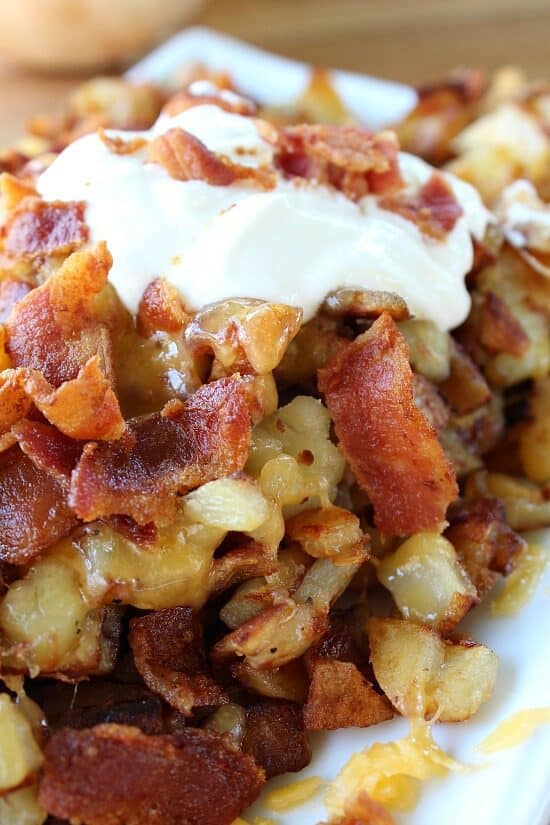 Fried cheesy breakfast potatoes with bacon on a white plate.