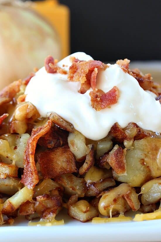 A serving of fried breakfast potatoes with bacon, cheese and sour cream on top.