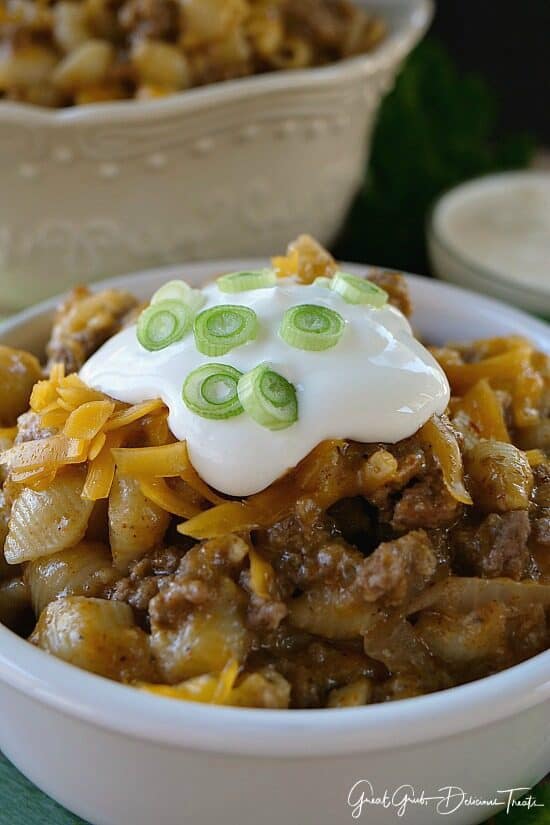 A white bowl filled with a serving of taco pasta with sour cream, cheese and green onions of top.
