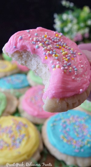 A close up of a pastel pink frosted sugar cookie with a bite taken out of it.