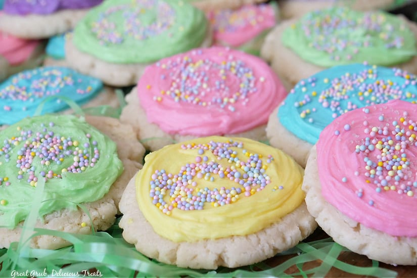 A horizontal photo of pastel frosted sugar cookies placed on Easter grass.