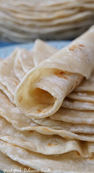 Flour tortillas in a stack with one rolled up at placed on top.