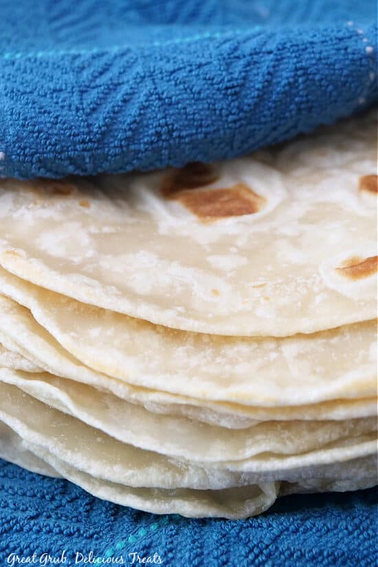 A close up photo of homemade flour tortillas placed on a blue kitchen towel to keep warm.