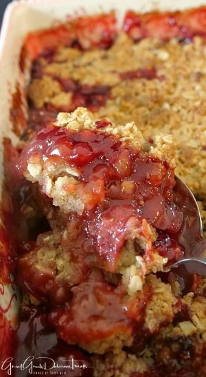 A baking dish with a large serving spoon scooping out a spoonful of homemade strawberry crisp.