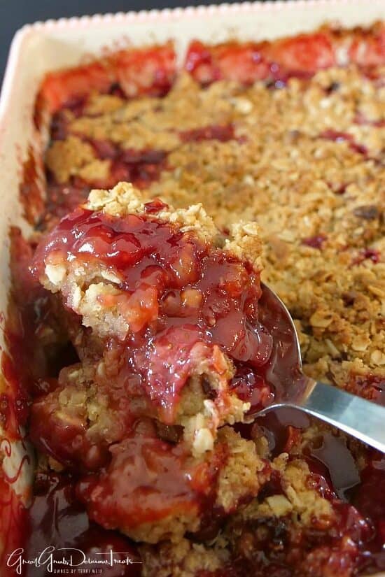 A baking dish with a serving spoon scooping out a serving of strawberry cobbler.