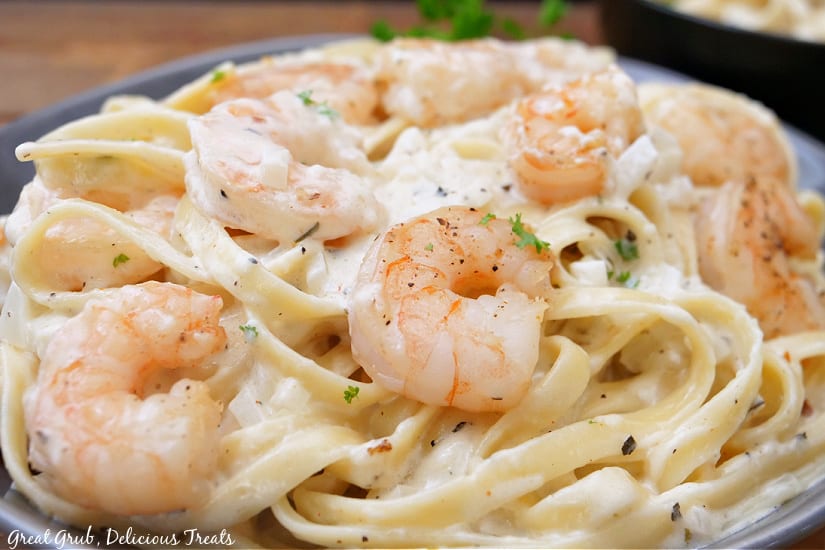 a horizontal photo of shrimp and fettuccine pasta in a creamy white sauce in a serving bowl.