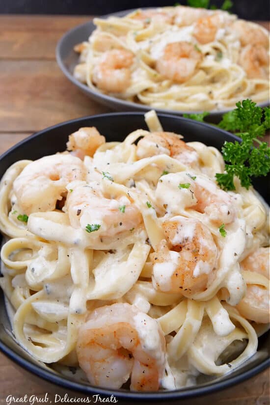 Two black bowls with a serving of shrimp and pasta in them.