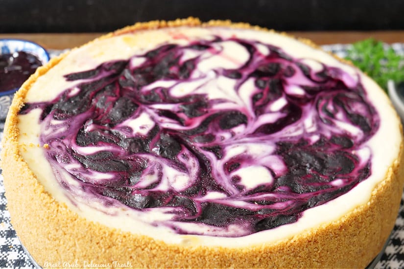 A whole blueberry cheesecake placed on a black and white checkered placemat.
