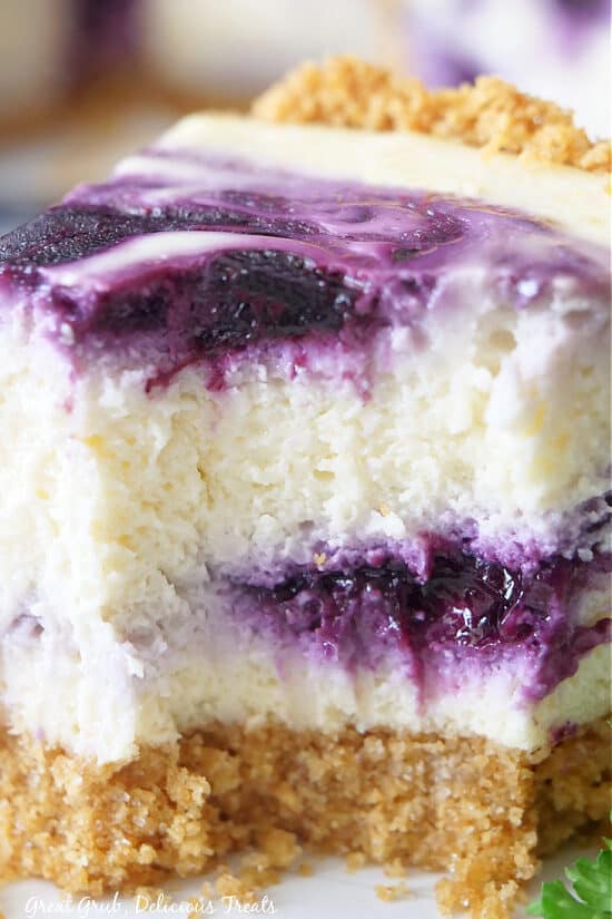 A close up slice of cheesecake with blueberry swirled in and on top of the cheesecake.