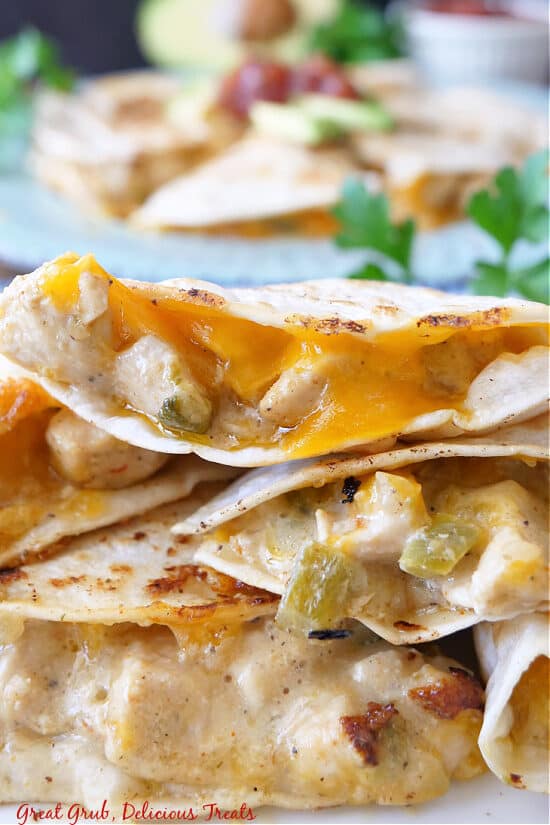A few pieces of chicken quesadilla stacked up, showing the cheese, chicken, peppers, and sauce that are in the middle. 