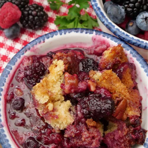 An overhead shot of a small bowl of cobbler with mixed berries in a small bowl in the background.