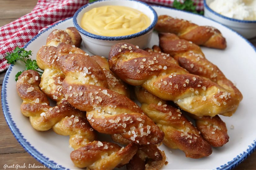 A large white plate with stacked soft pretzels on it with a small bowl of queso.
