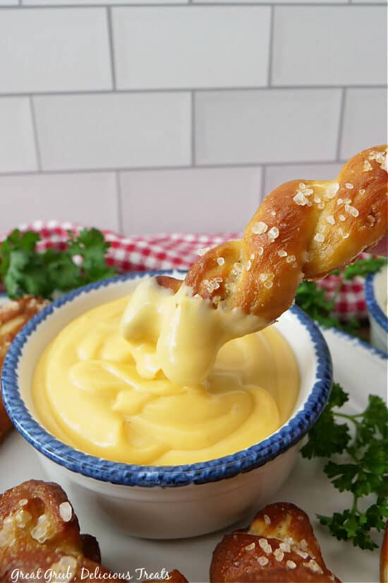 A soft pretzel being dipped into a small bowl of queso.