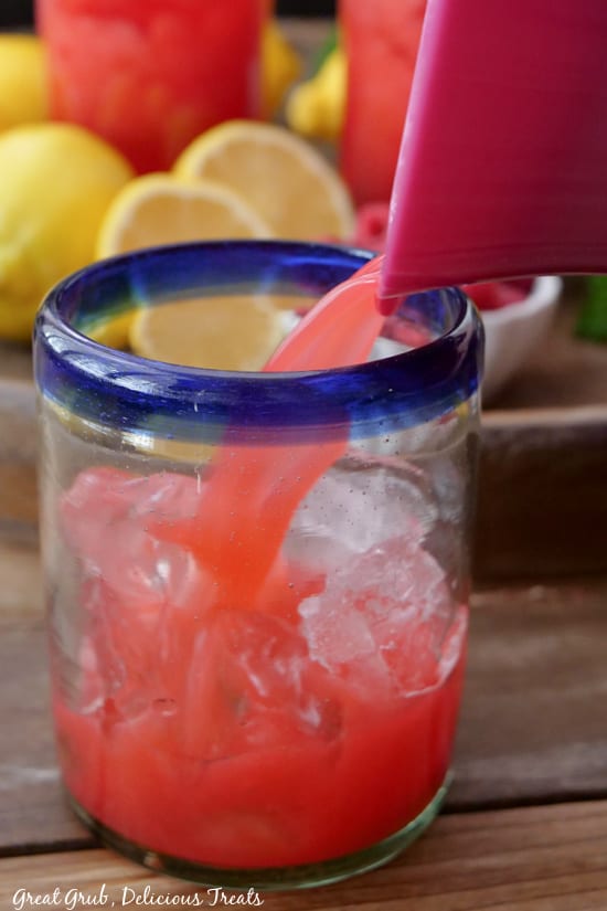 A glass filled with ice with raspberry lemonade being poured into the glass.