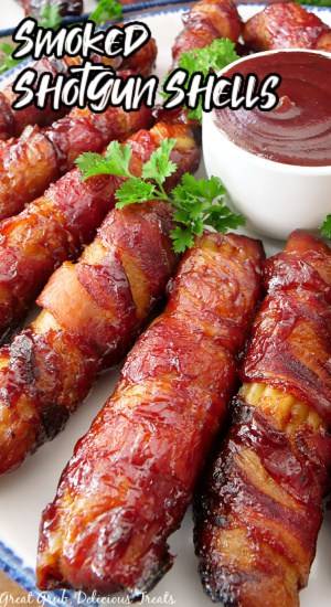 A white plate with blue trim with stuffed manicotti shells wrapped in bacon and smoked with a small  white bowl filled with barbecue sauce.