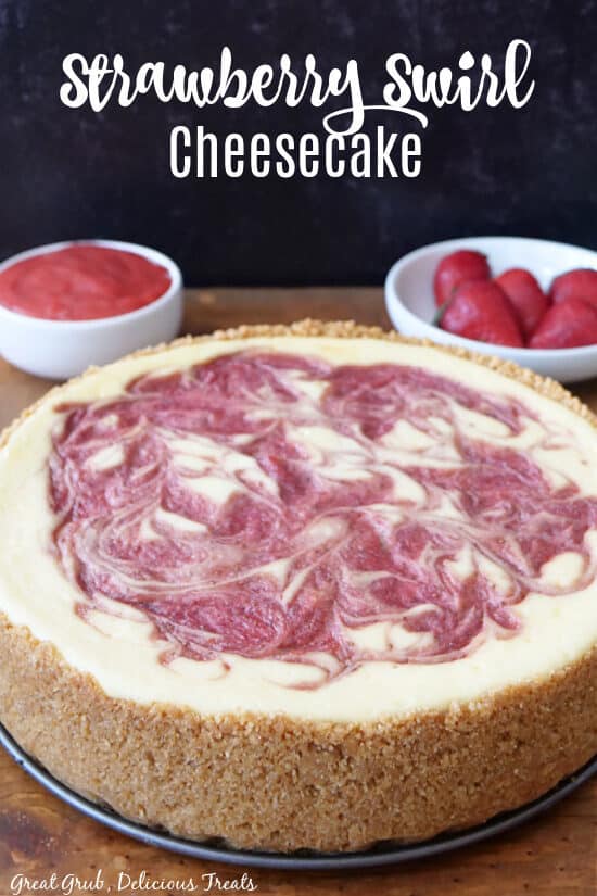 A whole cheesecake with a strawberry swirl on top in a graham cracker crust.