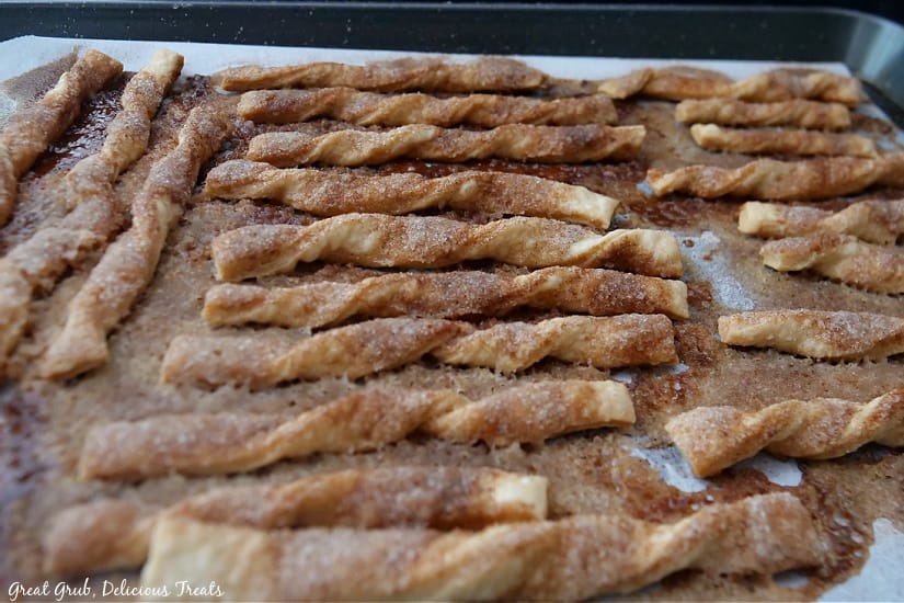 A baking sheet with a whole bunch of cinnamon twists on it after being baked.