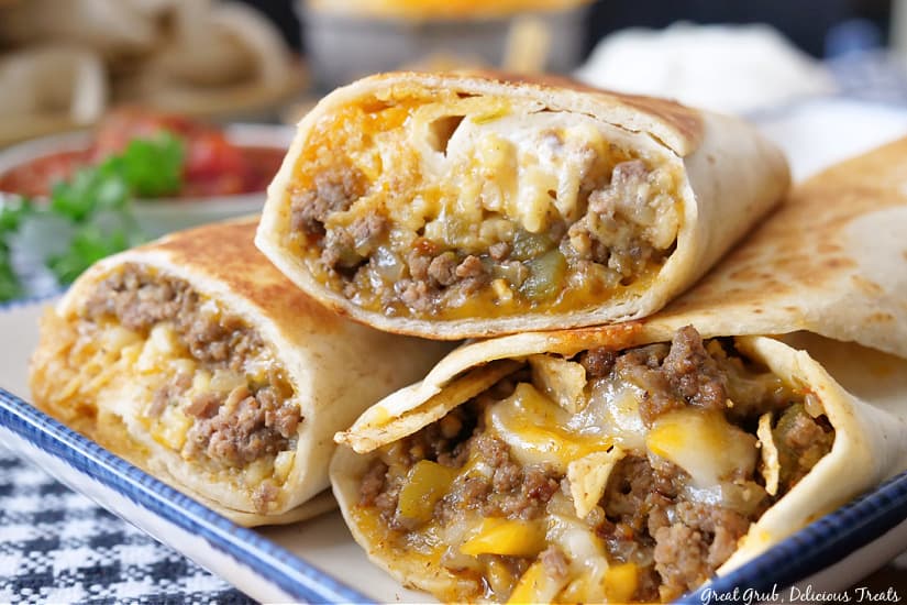 A horizontal photo of cheesy double beef burritos on a white plate with blue trim.