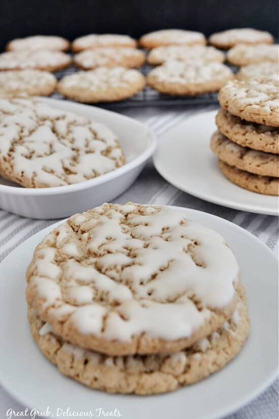 A white plate with two cookies, a plate in the background with four cookies, and a wire rack with a single layer of cookies on it.