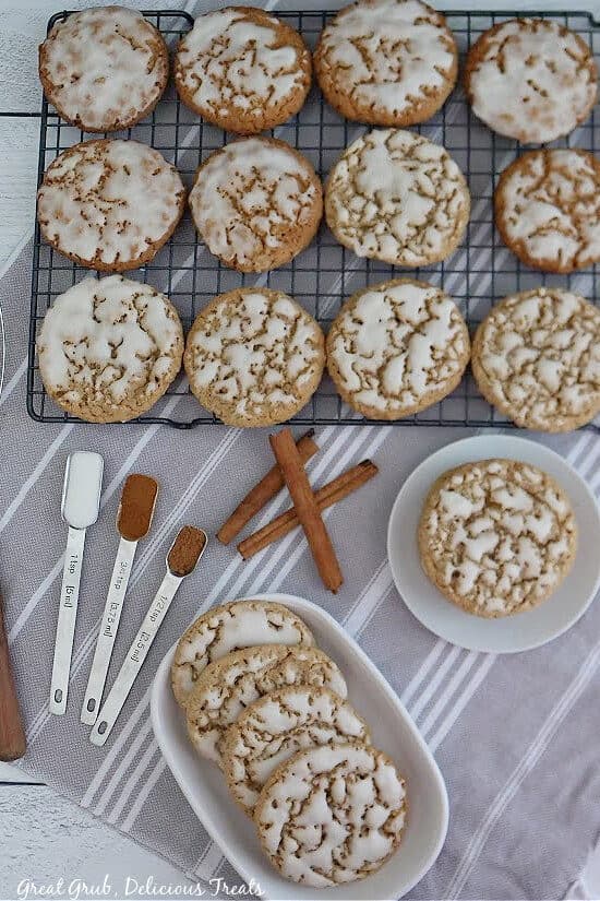 An overhead shot of oatmeal cookies on a wire rack with a small white dish filled with cookies, measuring spoons with spices, and three cinnamon sticks.